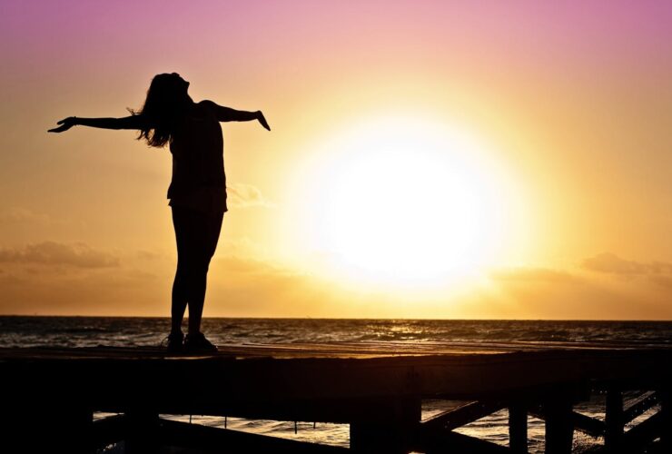 une femme heureuse et soulagée devant un couché de soleil